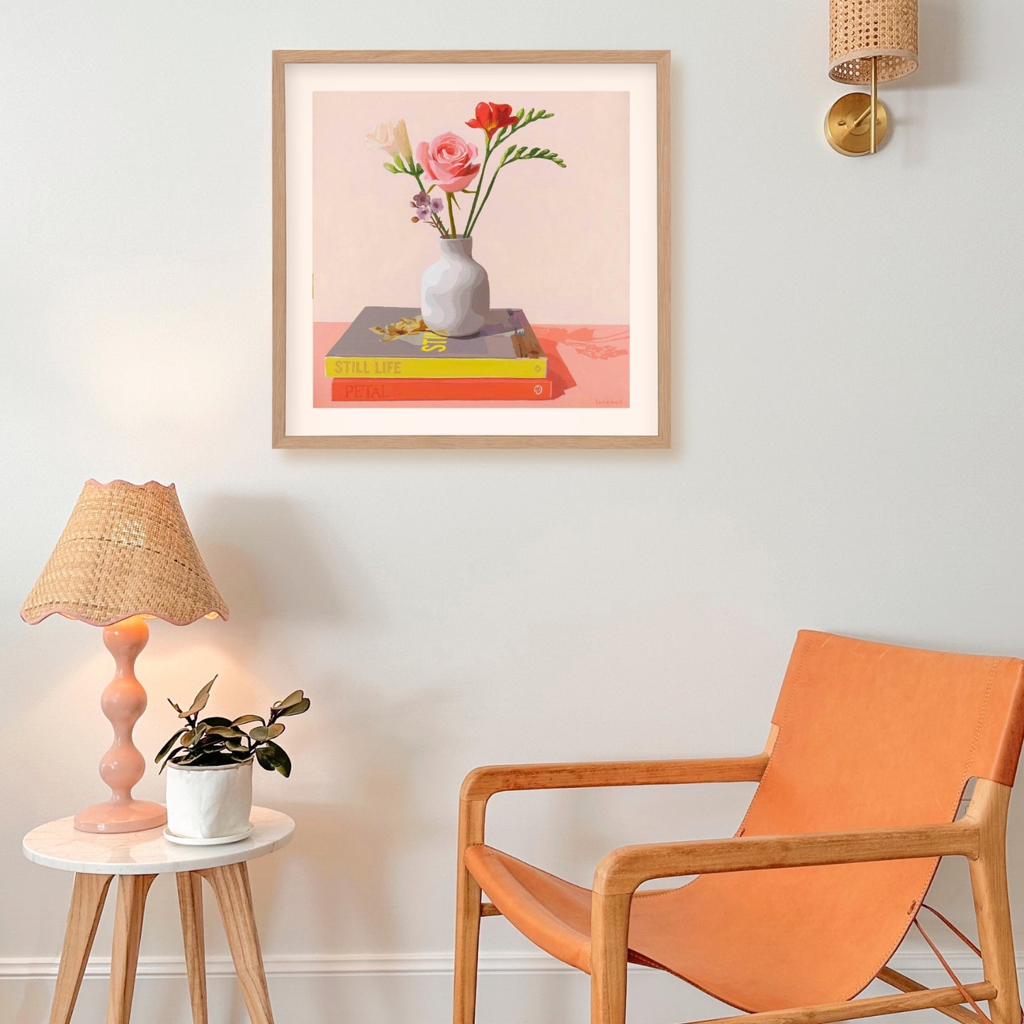 Framed artwork of flowers on books with a chair and lamp in a room.