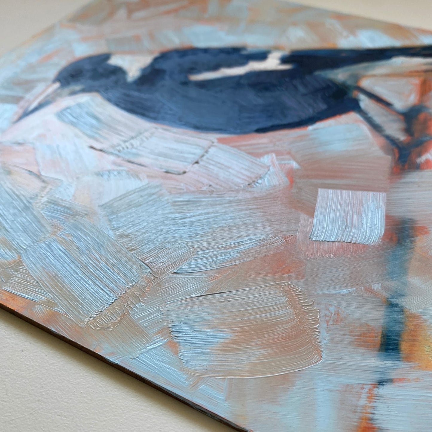 closeup of an original oil painting of a navy blue and white magpie on a textured sky blue background where you can see orange coming through
