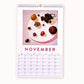 2024 art wall calendar in A3 size for the month of November, featuring a still life oil painting of fruits such as a plum, apricot, blueberries, raspberries, grapes, strawberries and blackberries on a creamy vanilla plate on a warm pink background