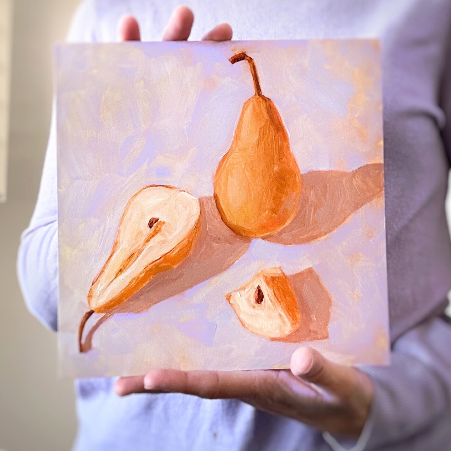 photo of a person holding an original oil painting of three deep yellow orange beurre Bosc pears on a textured lilac background