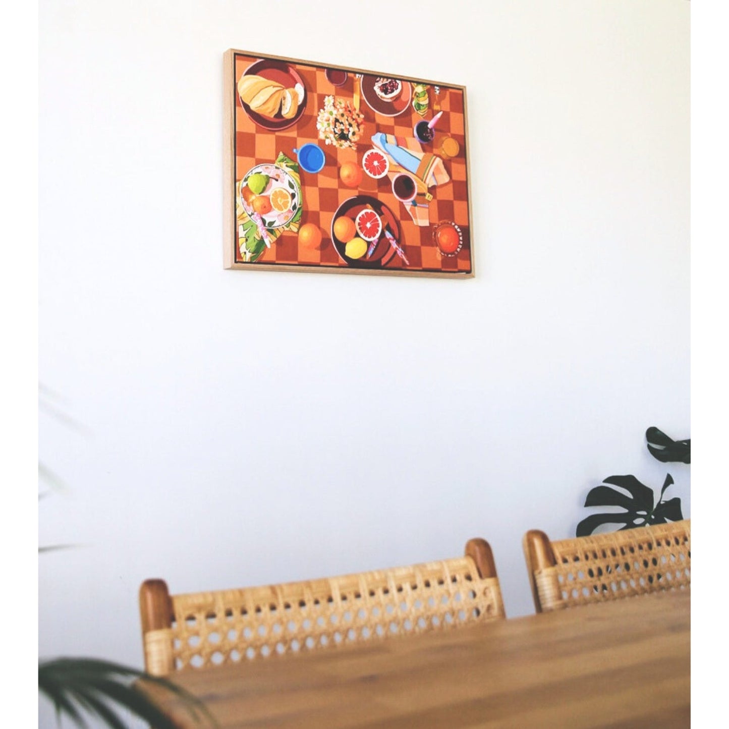 photo of a framed canvas print of a breakfast setup with oranges, lemons, tea towels, cutlery by kip and co, and flowers and cups on a chequered tablecloth background