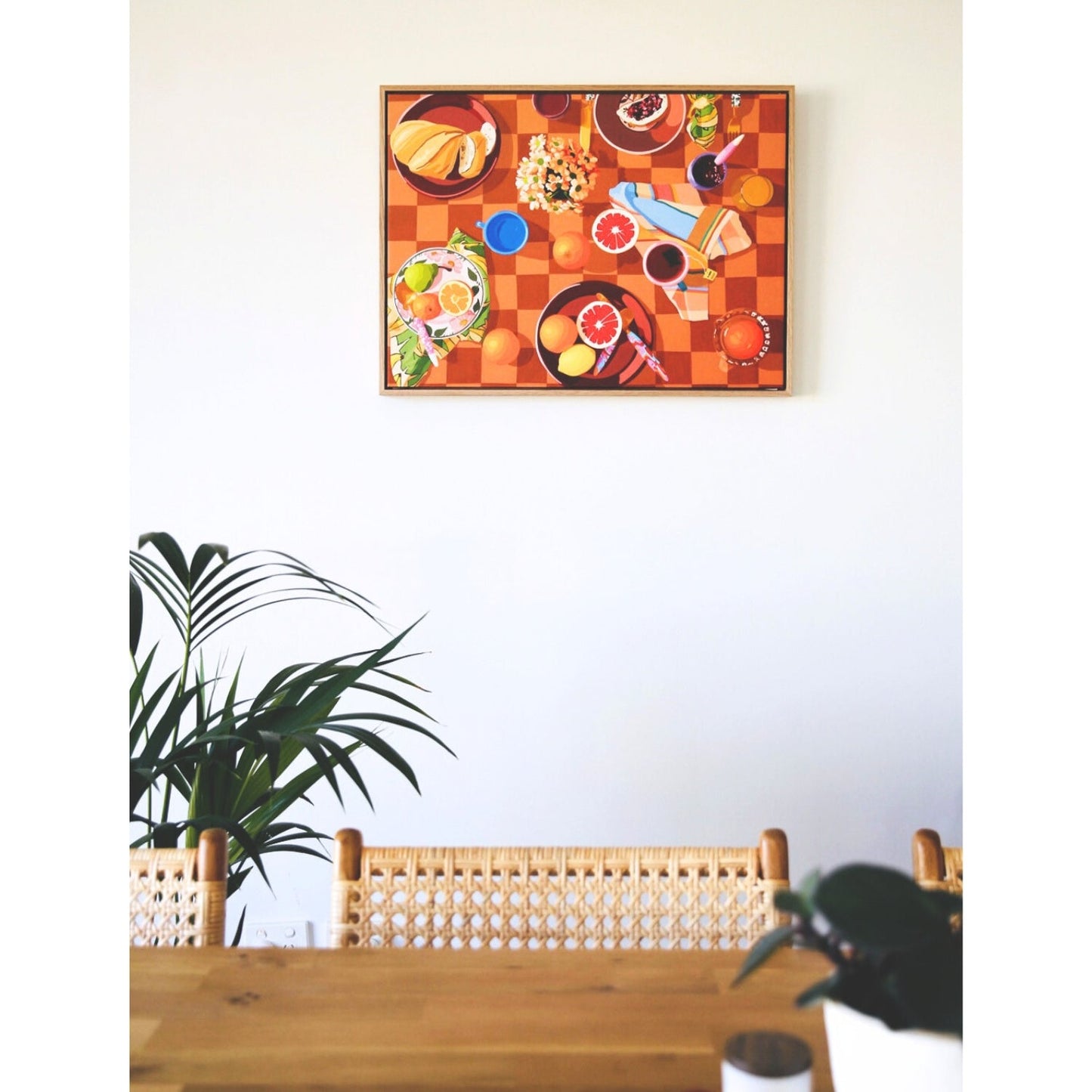 photo of a framed print of a breakfast setup with oranges, lemons, tea towels, cutlery by kip and co, and flowers and cups on a chequered tablecloth background