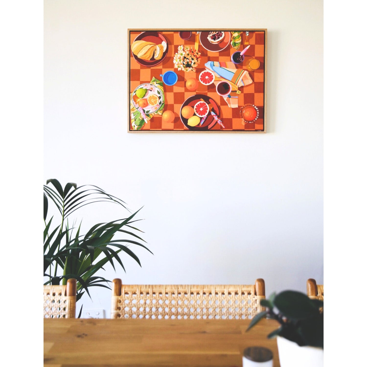 photo of a framed print of a breakfast setup with oranges, lemons, tea towels, cutlery by kip and co, and flowers and cups on a chequered tablecloth background