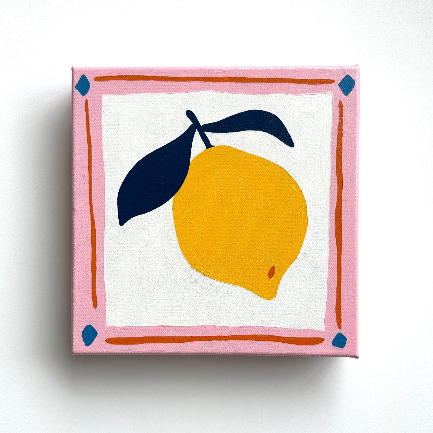 colorful modern and contemporary original oil artwork of a bright yellow lemon with navy blue leaves and a pink border by emerging australian artist yani lenehan