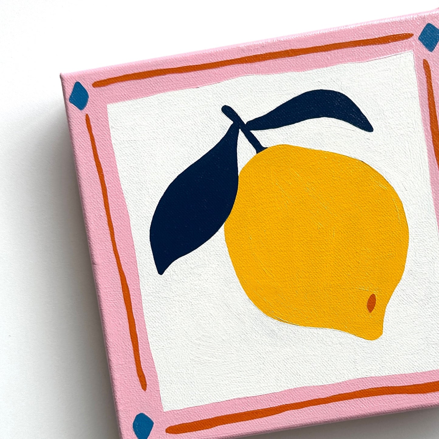 colorful modern and contemporary original oil artwork of a bright yellow lemon with navy blue leaves and a pink border by emerging australian artist yani lenehan