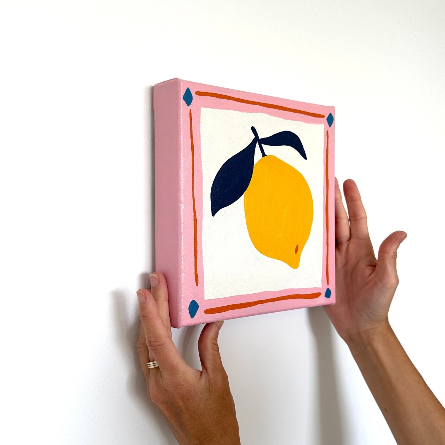 colorful modern and contemporary original oil artwork of a bright yellow lemon with navy blue leaves and a pink border by emerging australian artist yani lenehan