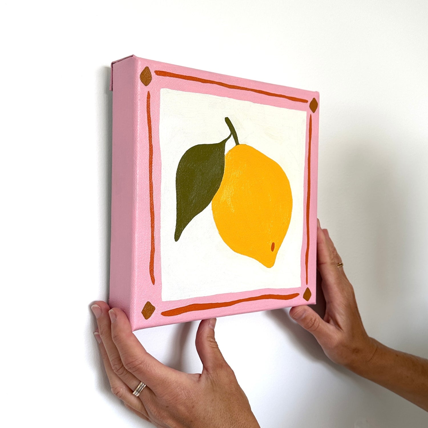 colorful modern and contemporary original oil artwork of a bright yellow lemon with olive green leaves and a pink border by emerging australian artist yani lenehan