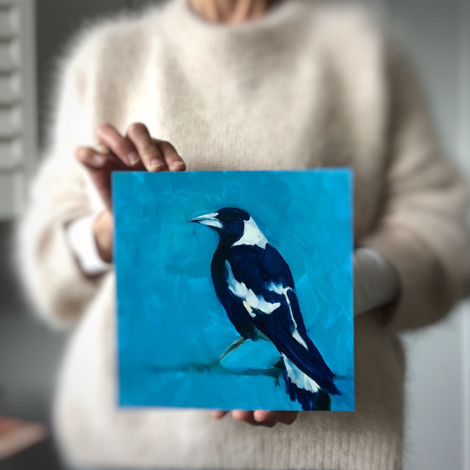 photo of a person holding an original oil painting of the profile of a navy blue and white magpie on a bright and textured turquoise background