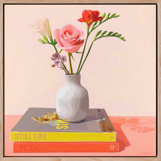 Framed artwork of a vase with flowers on books against a light creamy and peach background