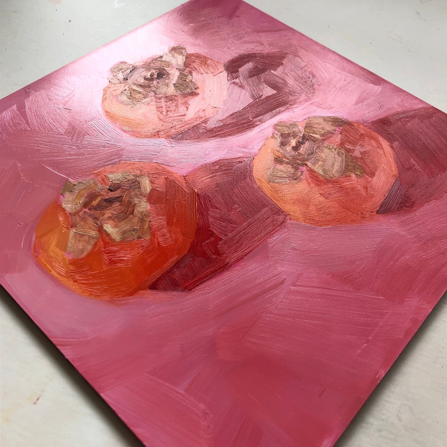 an original oil painting of three orange persimmons on soft pink with strong shadows