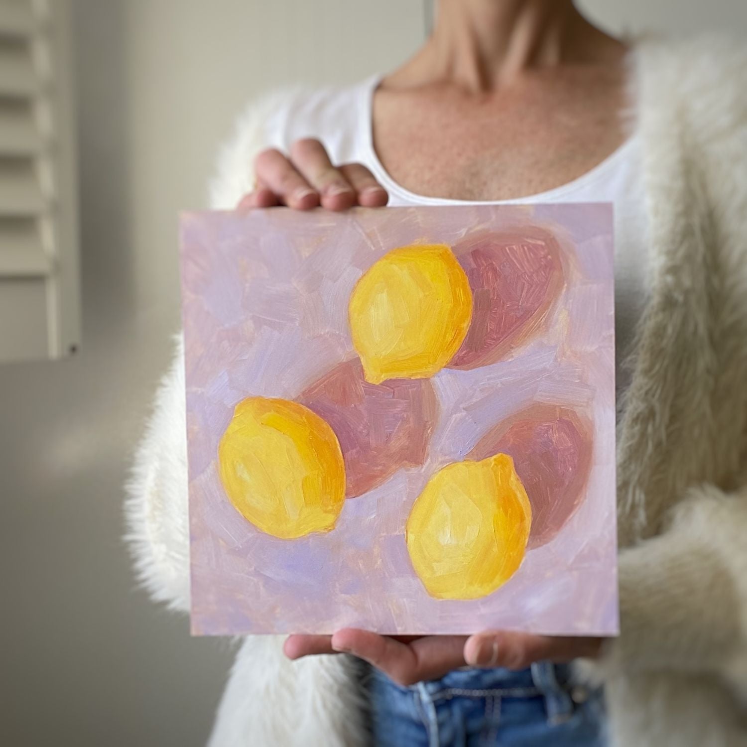 photo of a person holding an original oil painting of three vibrant lemons with strong dark pink shadows on a textured lilac background