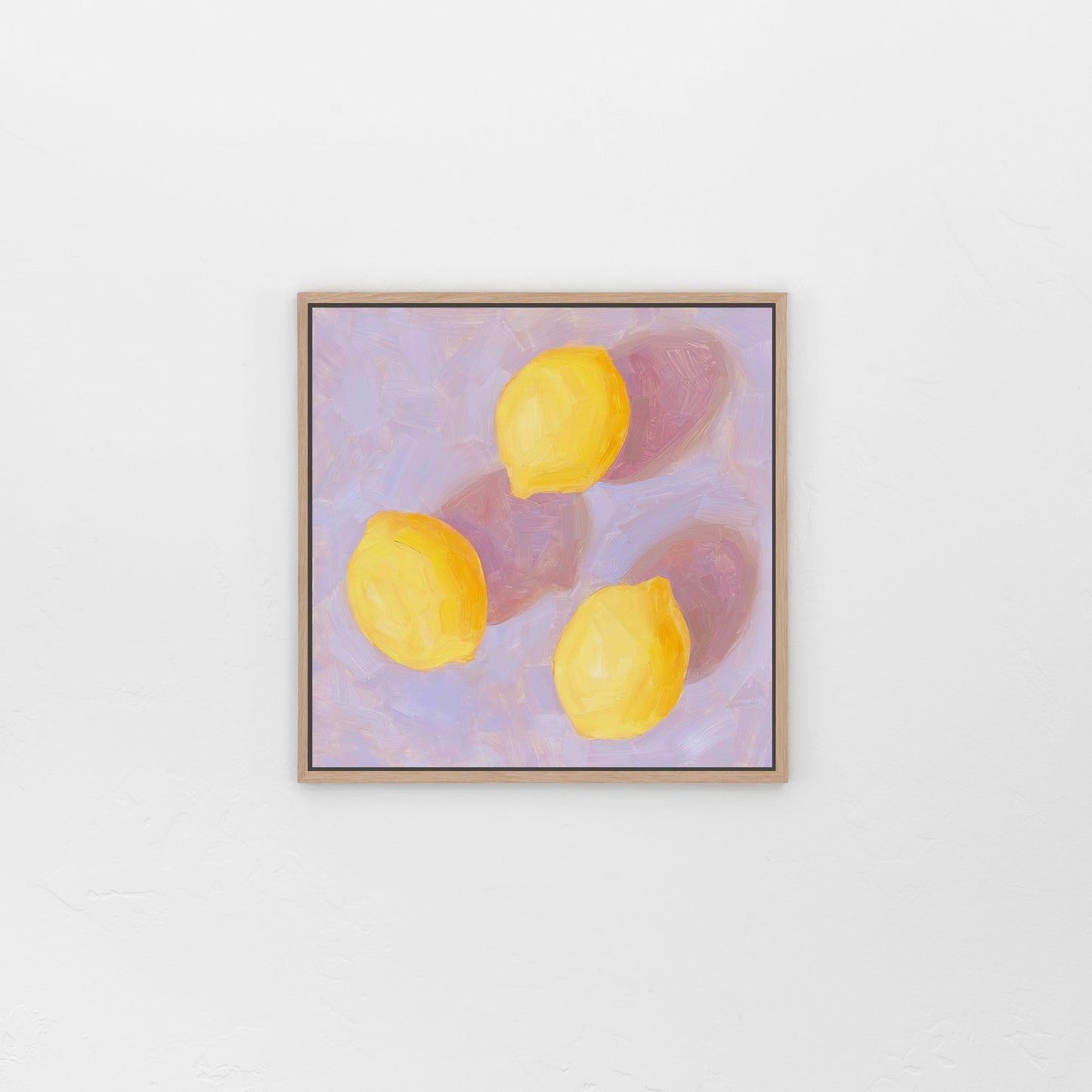 lifestyle photo of a framed canvas fine art paper print of an original oil painting of three vibrant lemons with strong pink shadows on a textured lilac background