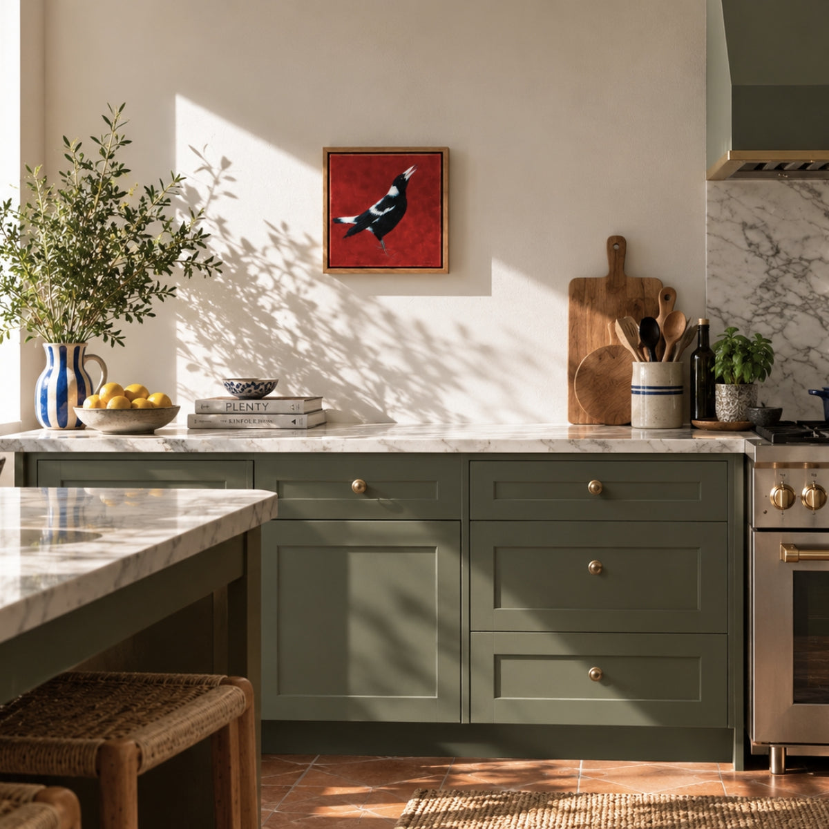 A styled kitchen interior with sage green shaker-style cabinets, a white marble countertop, warm wood tones, and a small framed red artwork of a magpie bird hanging on the wall. No person is present, but this is still not a clean isolated product shot; the real kitchen environment makes the best fit Lifestyle.