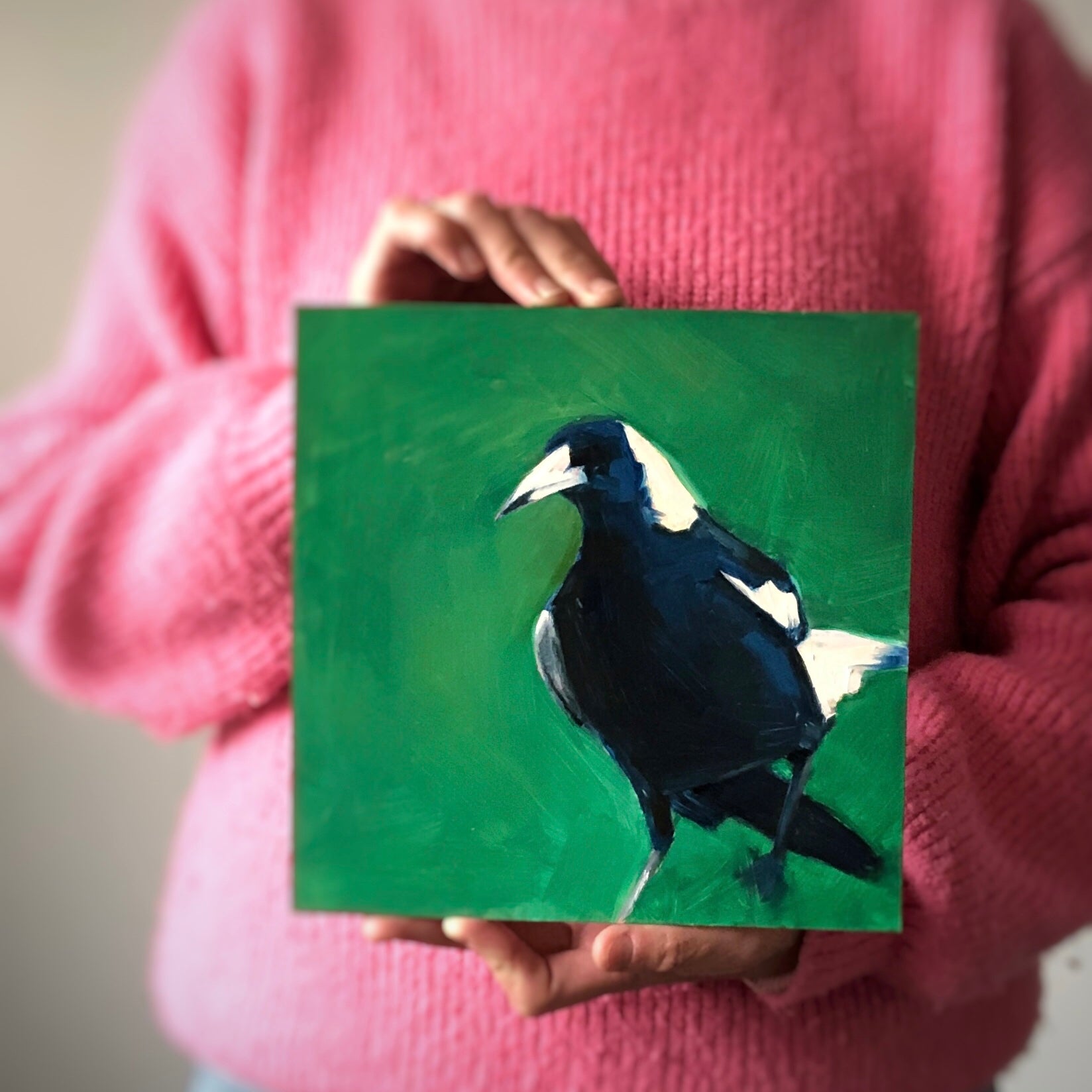 image of a person holding an original oil painting of a navy blue magpie on an emerald green background