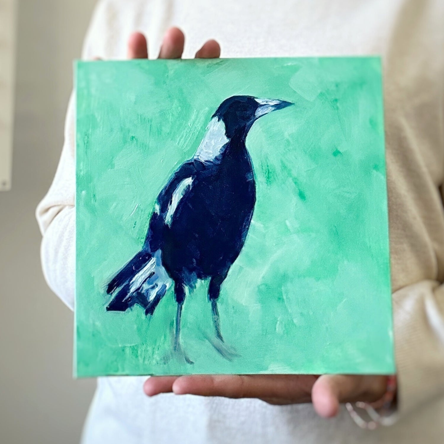 photo of a person holding an original oil painting of a navy blue and white magpie on a textured minty green background