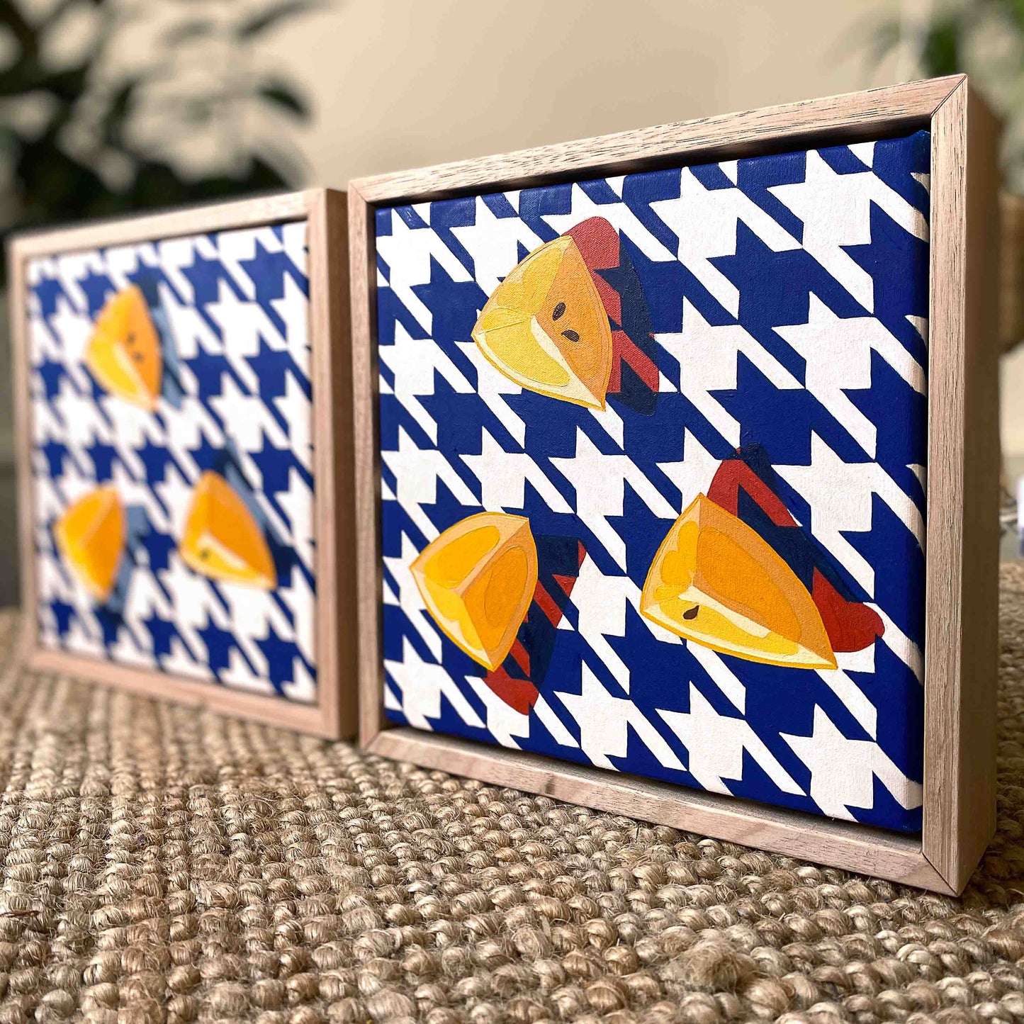 lifestyle photo of original oil paintings of three wedges of yellow lemons on a navy blue and white houndstooth background with strong red shadows, framed in a raw timber American Ash shadow box