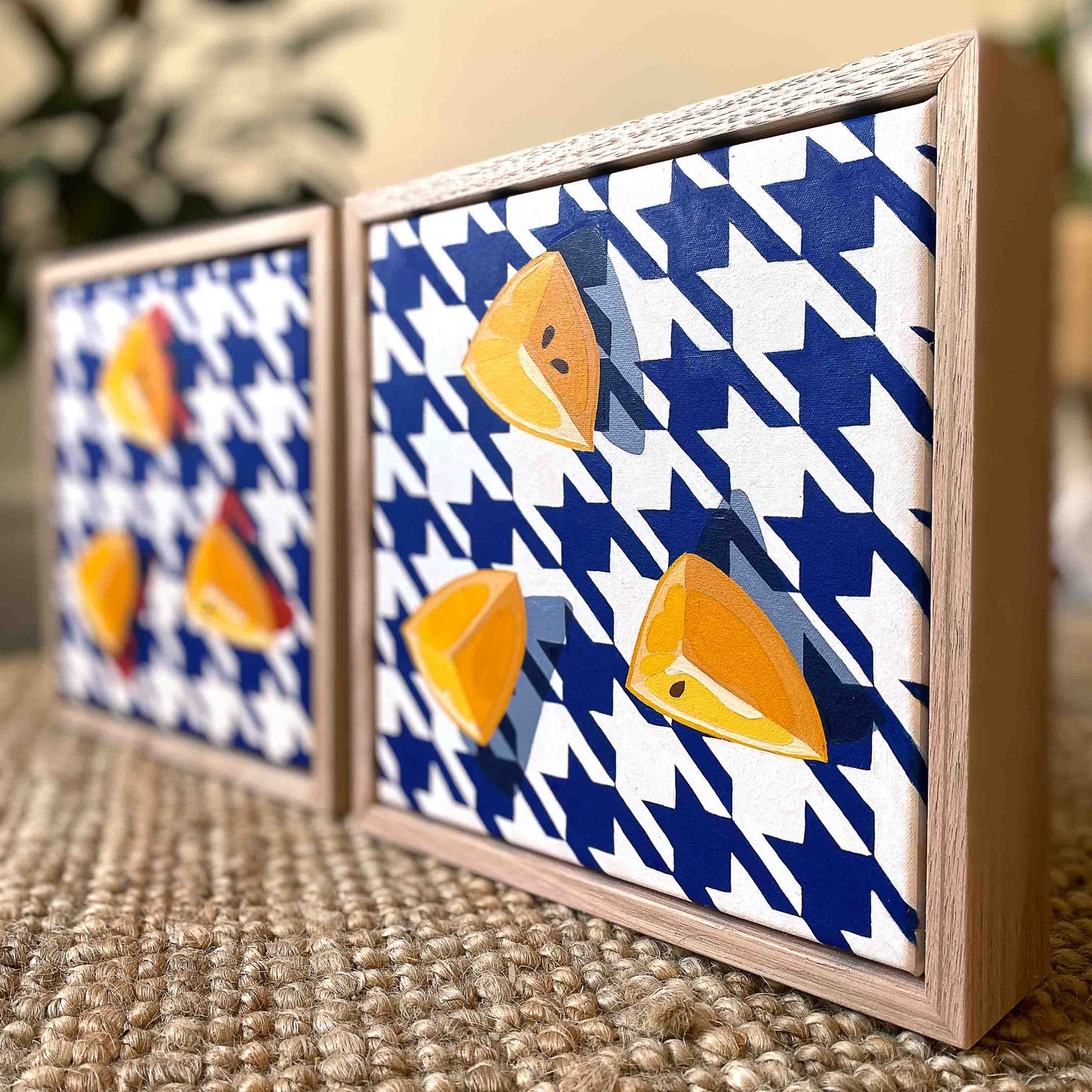 lifestyle photo of original oil painting of three wedges of yellow lemons on a navy blue and white houndstooth background with strong blue-grey shadows, framed in raw timber American Ash shadow box