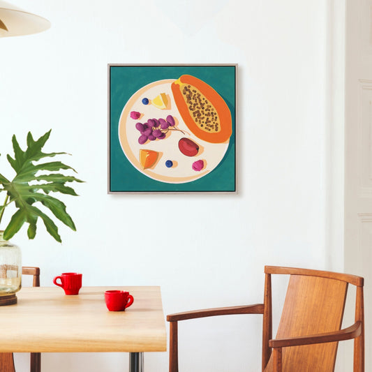Framed artwork of a fruit illustration on a wall above a wooden table with red cups.