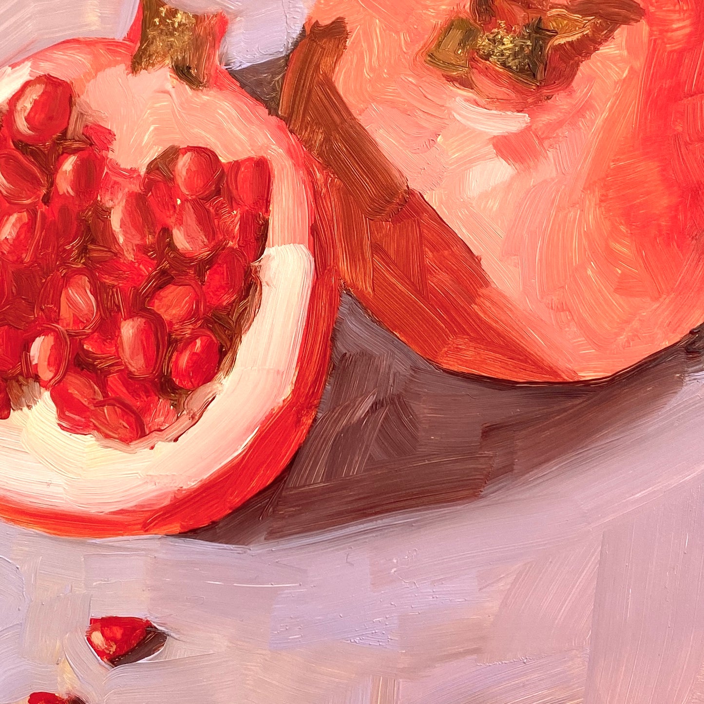 closeup of an original oil painting of a whole pomegranate and a cut pomegranate with seeds lying on a soft and smooth lilac background with bits of yellow showing through