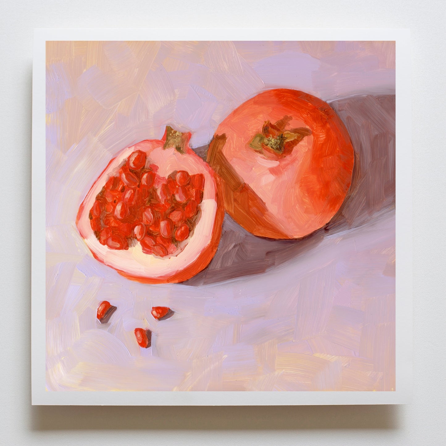 photo of a fine art paper print on board of a full pomegranate and a cut pomegranate and seeds on a textured soft lilac background