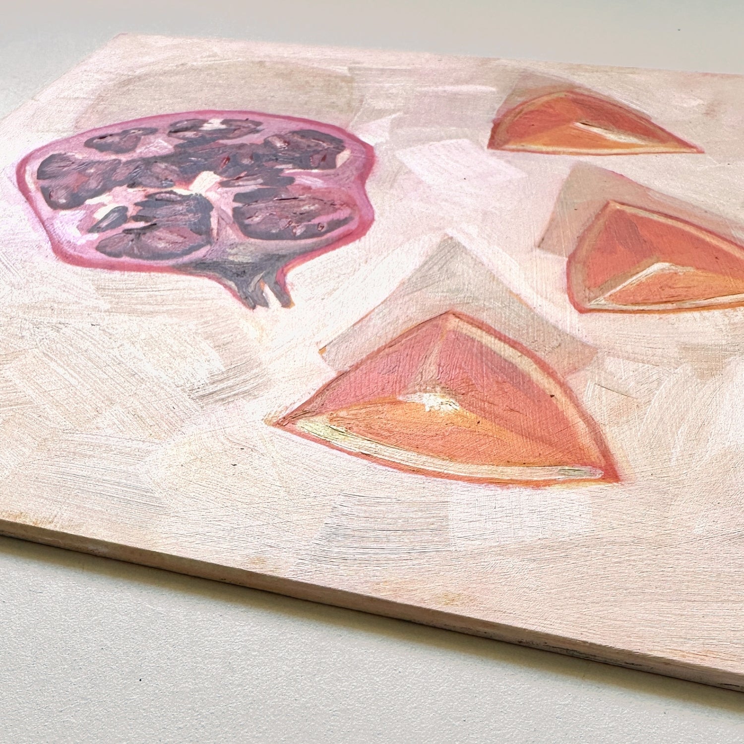 closeup of an impressionistic original oil painting of a still life setting of pomegranate fruit and three orange slices on a textured cream background with soft shadows