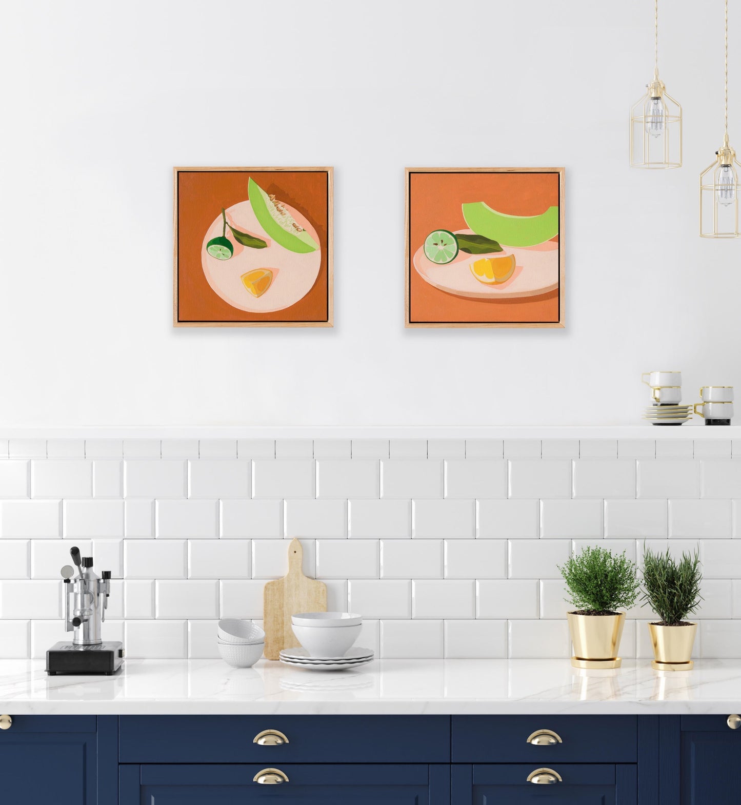 lifestyle image of a kitchen showing two original oil paintings of a slice of honeydew melon, a wedge of lemon and half a lime with leaves on a cream coloured plate, with very light warm pink shadows, sitting on chai coloured background, framed in American ash shadow box, hanging on a white wall